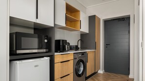 A compact kitchen with a Bosch microwave, DEFI refrigerator, and a washing machine. - On Park | Modern Century City Studio (Cape Town)