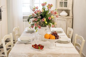 A dining table set with plates, cutlery, a vase of flowers, and a bowl of fruit. - LUXURY APARTMENT SUITE LA FONTANA (Lucca)