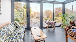 A conservatory with a sofa, table, and chairs, surrounded by potted plants and a view of the garden. - 3 bedroom accommodation in Castle Martin, near Pembroke (Castle Martin, near Pembroke)