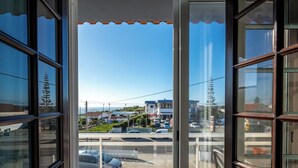 Une vue depuis une fenêtre, avec un ciel dégagé, un parking et des bâtiments visibles au loin.