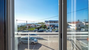 Une vue depuis une fenêtre donnant sur un parking où sont garées plusieurs voitures, un bâtiment avec un toit bleu et un ciel dégagé.