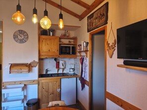 Compact kitchen with microwave, coffee maker, and sink, featuring a television and hanging light fixtures.