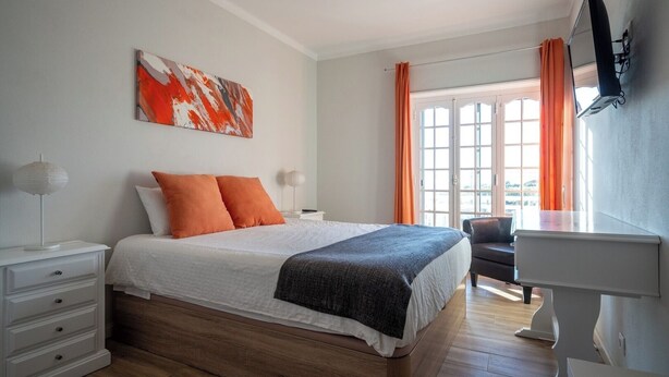 Ein Schlafzimmer mit einem Bett, einem Schreibtisch, einem Stuhl, einem Fernseher und einem Fenster mit Vorhängen.