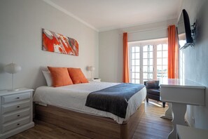 Een slaapkamer met een bed, een bureau, een stoel, een televisie en een raam met gordijnen.