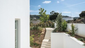 Et moderne udendørs område med en betontrappe, der fører op til en have, omgivet af hvide vægge og forskellige planter.