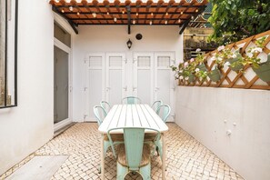A patio with a wooden table and chairs, a pergola with string lights, and a white wall with a wooden lattice. - Close to all the magical places in Sintra. (Sintra)