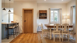 A dining area with a wooden table and chairs, a kitchen area with a bar counter and stools, and a wooden door. - Close to all the magical places in Sintra. (Sintra)