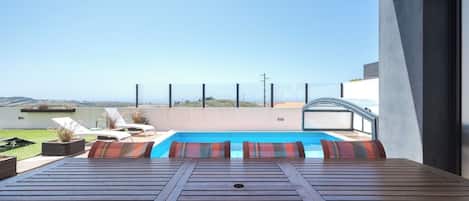 Uma piscina no terraço com vista para o oceano, cadeiras de descanso e design arquitetônico moderno.