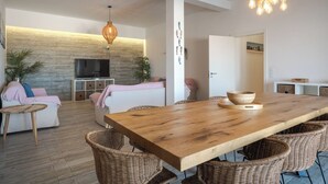 Un salon moderne avec une table à manger en bois, des chaises en osier, un téléviseur et un mur en pierre.