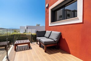 A balcony with a wooden table and a grey sofa.
