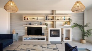 Un salon moderne doté d’un téléviseur à écran plat, d’une cheminée et de deux lampes suspendues en osier.