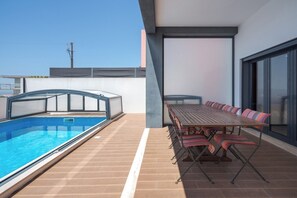 Un espace piscine sur le toit, doté d’une piscine couverte, d’une table à manger avec des coussins à rayures et d’une vue sur le panorama urbain.