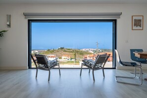 A room with a large sliding glass door leading to a view of a coastal town. - Ocean Spirit - Ericeira with stunning views (Carvoeira)