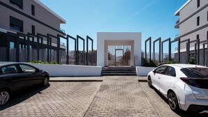 A modern building with a central entrance, two cars parked in front, and a paved driveway.