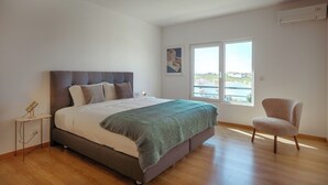 A bedroom with a bed, a chair, a nightstand, and a window with a view.