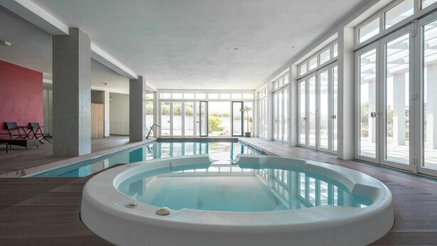 An indoor swimming pool with a hot tub, large windows, and a view of the outdoors.