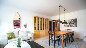A modern living room with a white sofa, a dining table with chairs, a wooden cabinet, and a zebra print artwork on the wall.