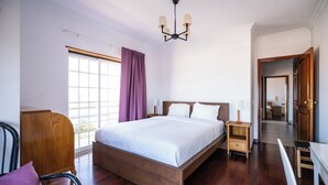 A modern hotel room with a large bed, wooden flooring, a desk, and a chair.