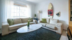 A modern living room with two beige sofas, a round coffee table, a potted plant, and a surfboard decoration on the wall.