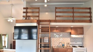A compact kitchen with a lofted sleeping area, a built-in TV, and a gas stove.
