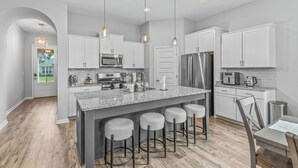 A modern kitchen with white cabinets, a granite countertop, stainless steel appliances, and bar stools.