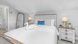 A neatly made bed with a swan-shaped towel, a bedside table with a lamp, and a nightstand with a clock.