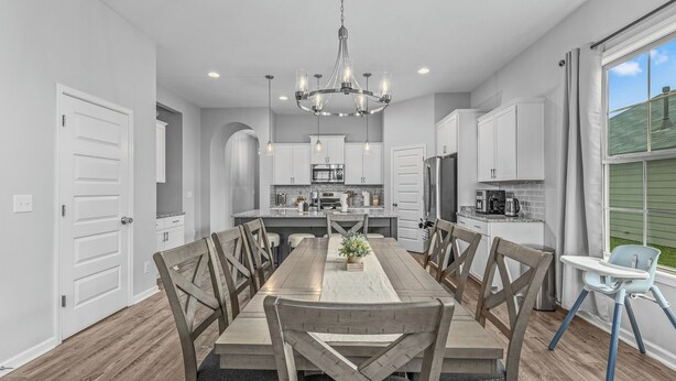 A modern kitchen with white cabinets, a central island, and a dining area with a wooden table and chairs.