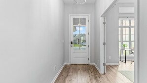 A hallway with a white door, wooden flooring, and a view of a house through the door.