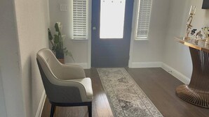 Un couloir avec une chaise, un tapis, une porte et une console ornée d’objets décoratifs.