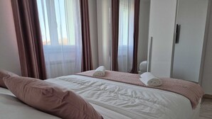 A neatly made bed with white and pink bedding, a pink throw blanket, and two rolled towels. - Cozy apartment near the Sea with all amenities. (Citta Sant' Angelo)