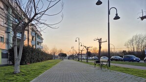 A paved pathway lined with street lamps and benches, leading towards a building with a flat roof and multiple windows. - Cozy apartment near the Sea with all amenities. (Citta Sant' Angelo)