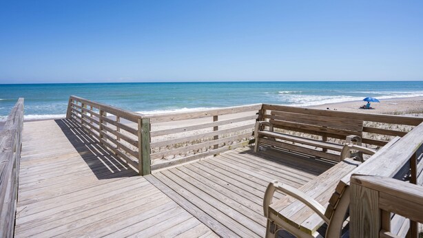 A wooden pier leading to a beach with a bench and a table. - Ocean view condo in Surf City! (Surf City)