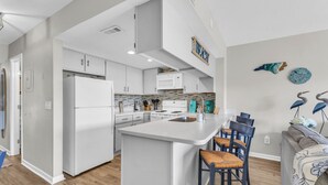A modern kitchen with white cabinetry, a central island, and bar stools. - Ocean view condo in Surf City! (Surf City)