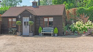 A rustic wooden house with a gravel driveway, a bench, and potted plants. - Rose Cottage - UK49048 (Banstead)