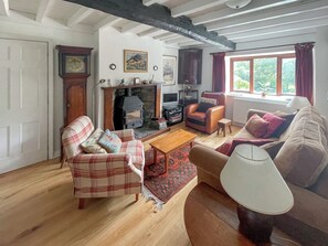 Un salon chaleureux avec une cheminée, des meubles à motifs écossais et une vue sur la verdure environnante.