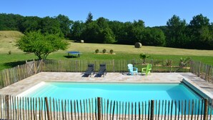 A rectangular swimming pool with a wooden fence, two lounge chairs, and a single chair. - L'écrin du Val de Louyre, in the heart of Périgord Noir, with private pool (Val de Louyre et Caudeau)