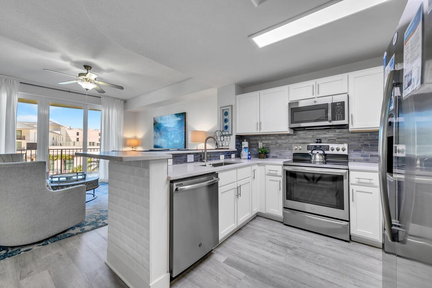 A modern kitchen with white cabinets, stainless steel appliances, and a grey island.