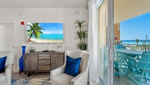 Ein Zimmer mit Blick auf den Strand, ein Holzkabinett, ein Sessel mit blauer Sitzkissen und ein Tisch mit Stühlen.