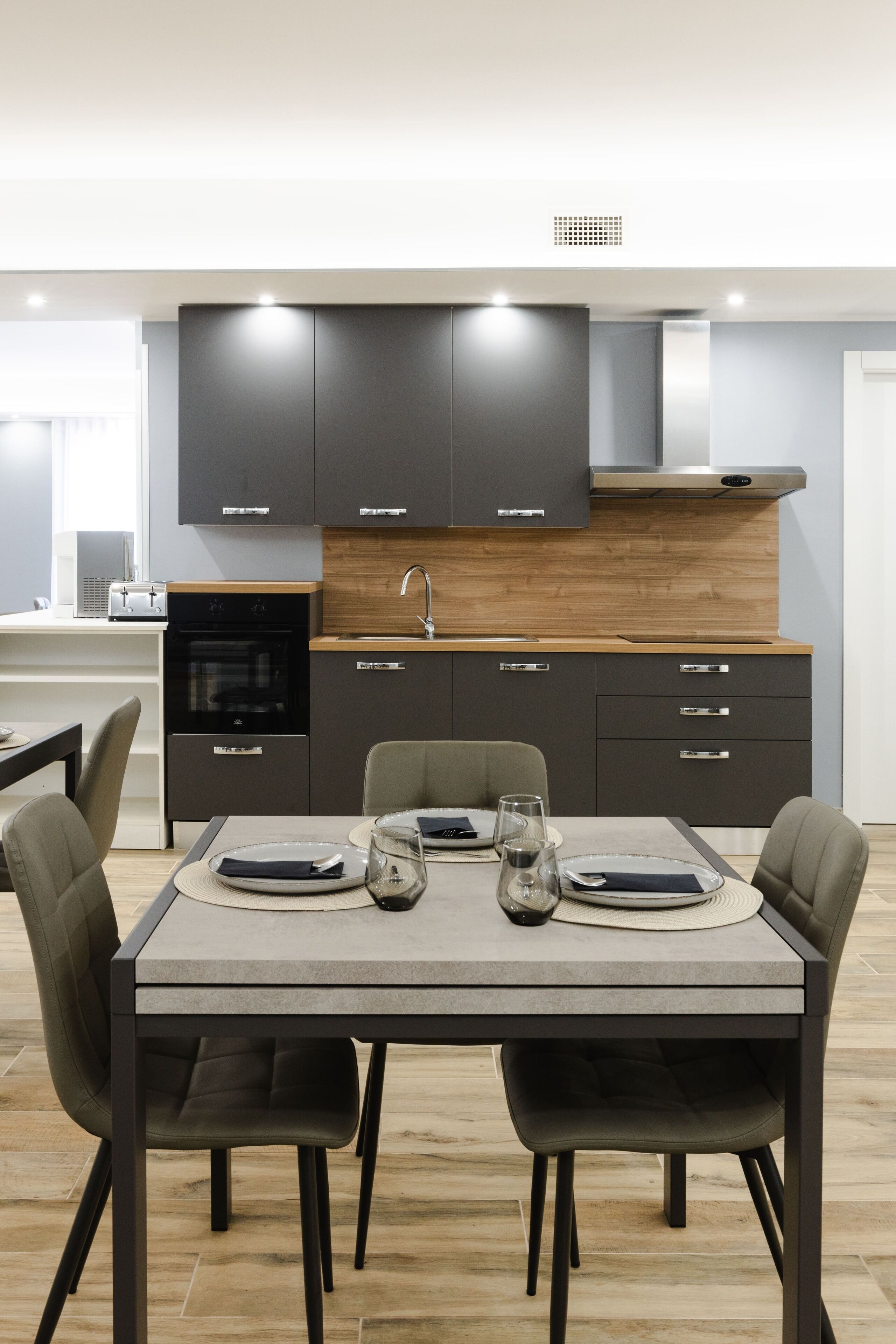 Una cocina moderna con armarios oscuros, encimera de madera y comedor con una mesa dispuesta para dos personas.