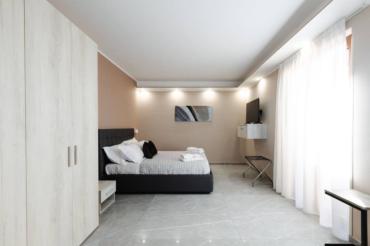 A modern bedroom with a bed, a wardrobe, a bedside table, and a wall-mounted TV.