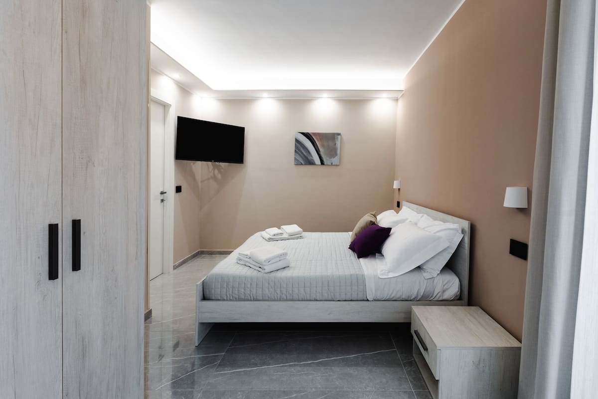 A modern bedroom with a bed, bedside table, and a TV mounted on the wall.