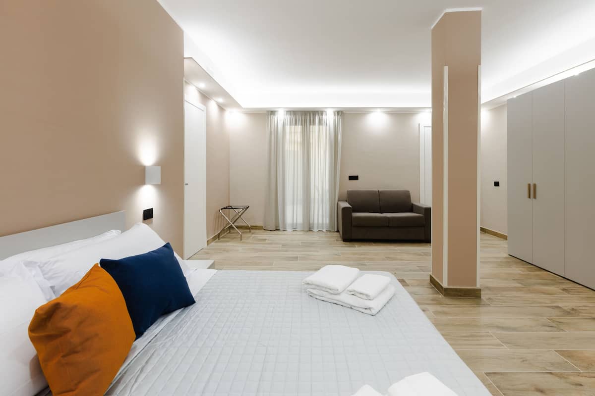 A modern hotel room with a large bed, a sofa, and a wardrobe.