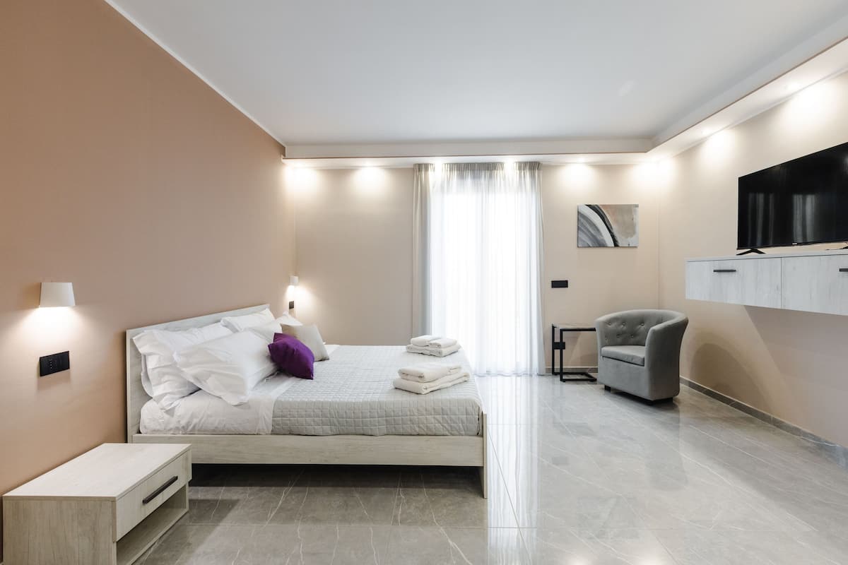 A modern bedroom with a bed, bedside table, chair, and a flat-screen TV mounted on the wall.