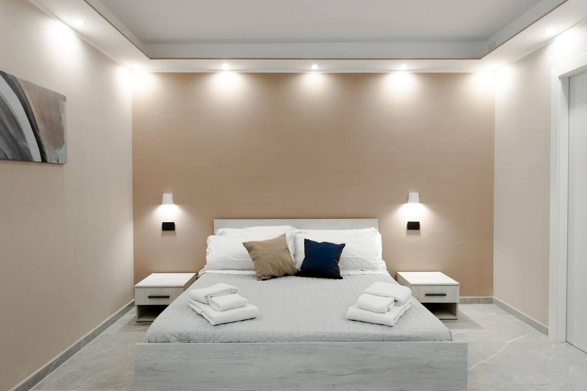 A modern bedroom with a bed, two bedside tables, and wall-mounted lights.