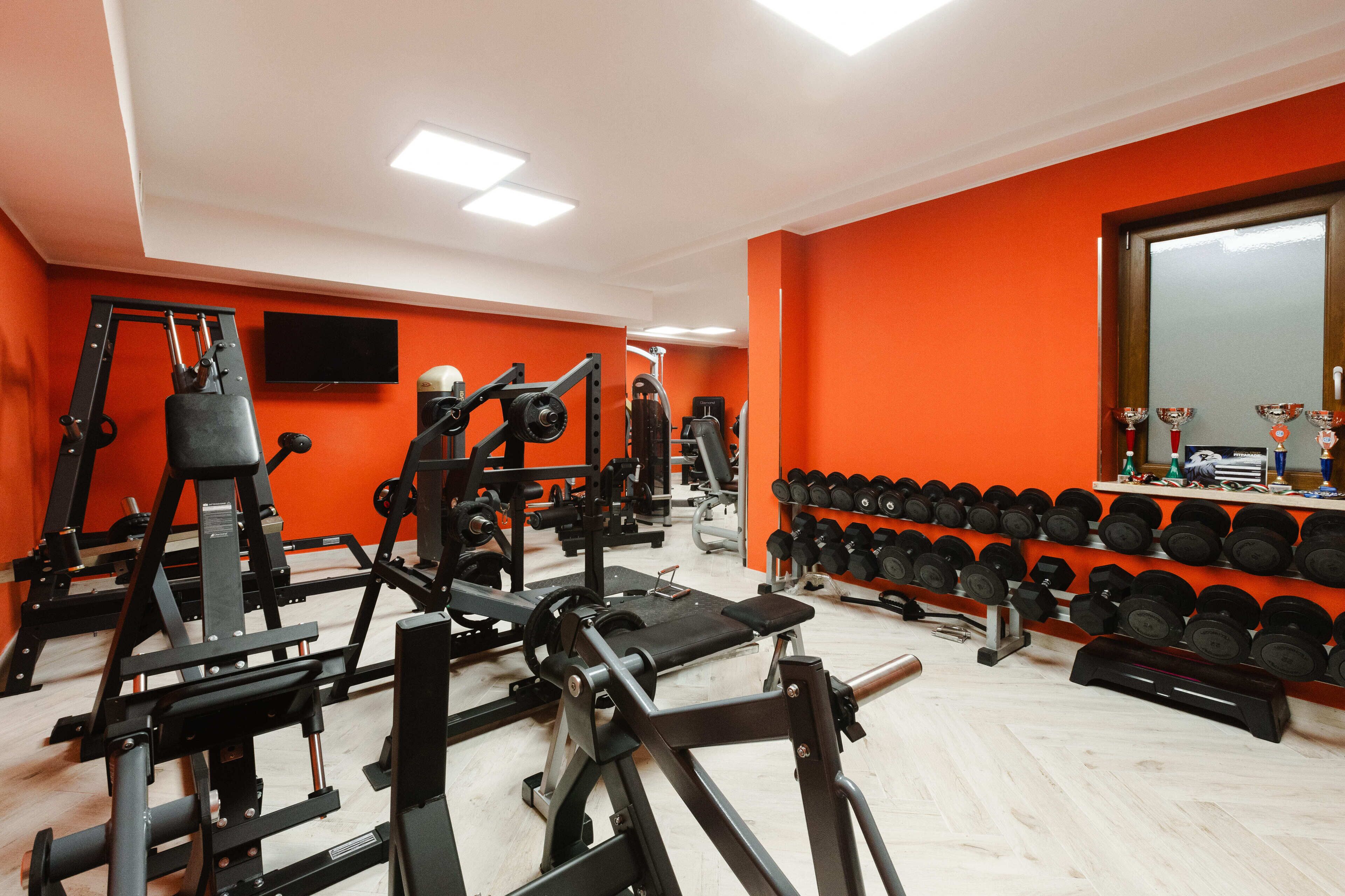 Ein Fitnessraum mit unterschiedlichen Trainingsgeräten, einem an der Wand befestigten Fernseher und einem Hantelgestell.