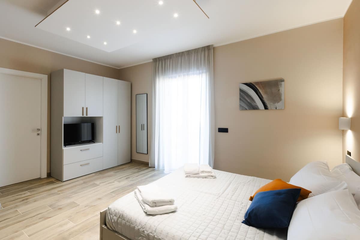 A modern hotel room with a large bed, a television, a wardrobe, and a window with curtains.