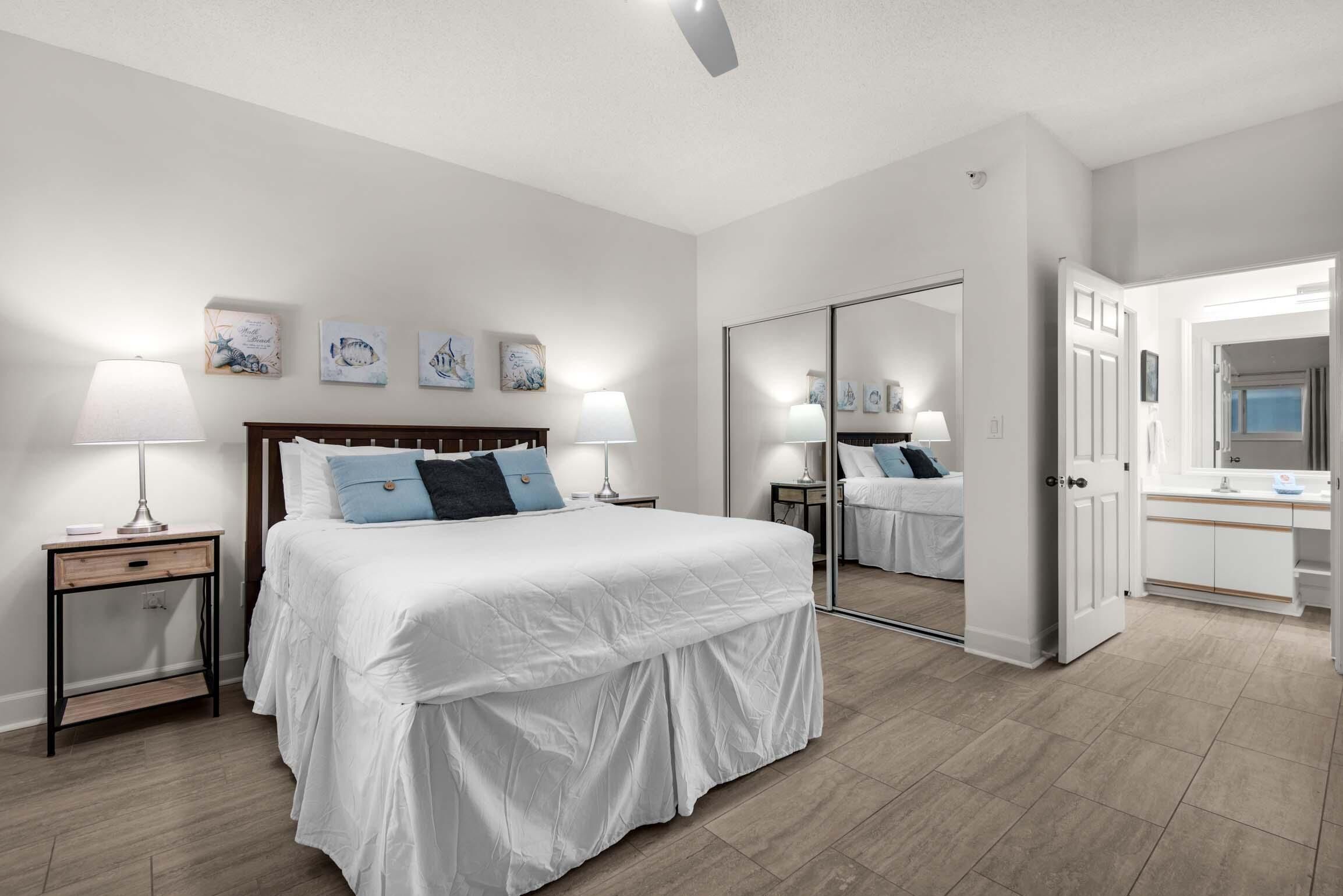 Un dormitorio con una cama grande, mesitas de noche, un espejo y un baño con lavamanos y espejo.