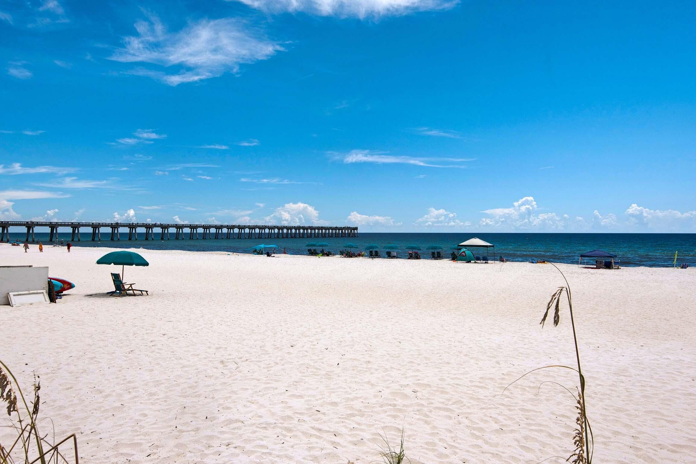 A beach with a pier extending into the water, sun loungers, and umbrellas.