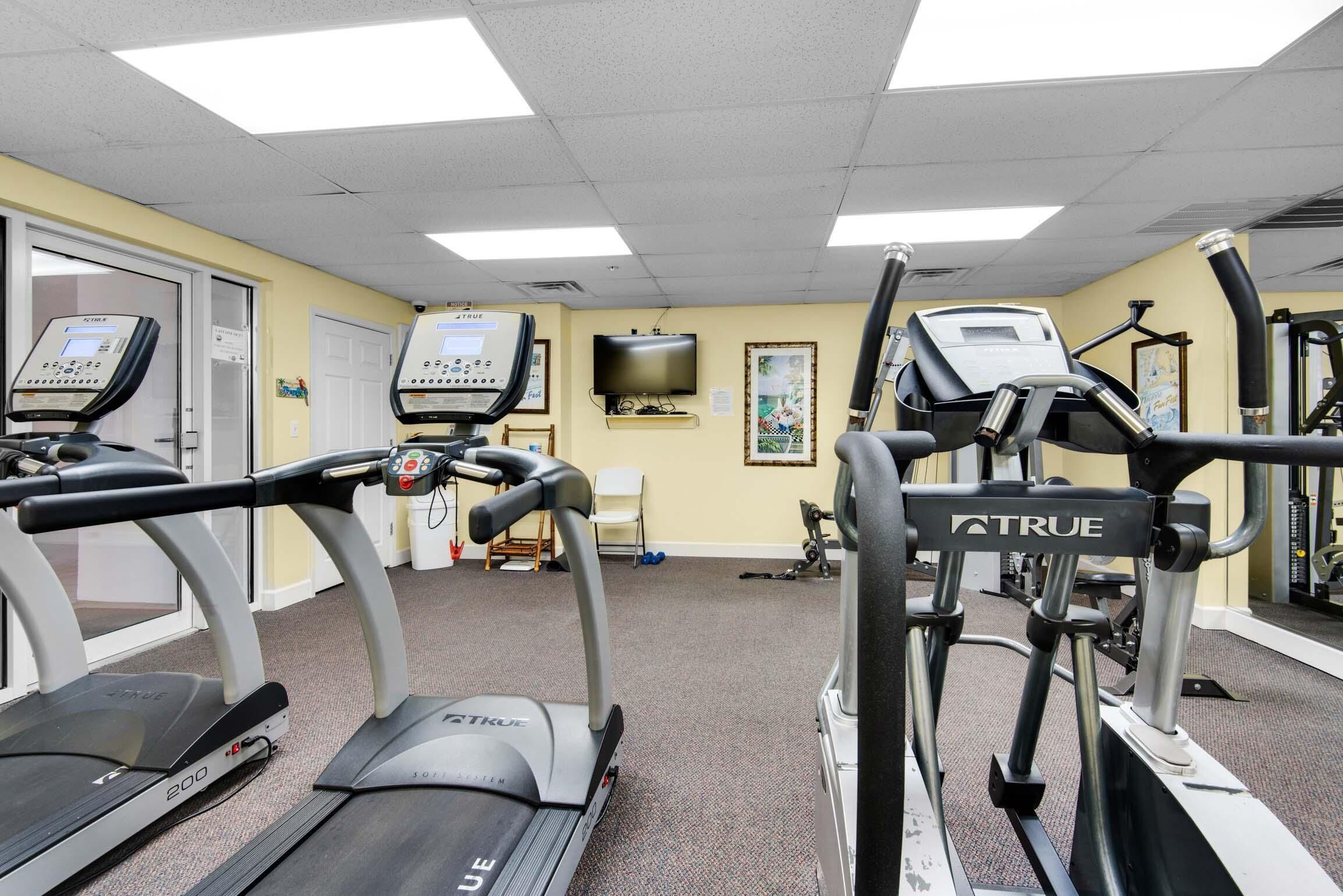 A fitness center with treadmills, exercise bikes, and a TV on the wall.