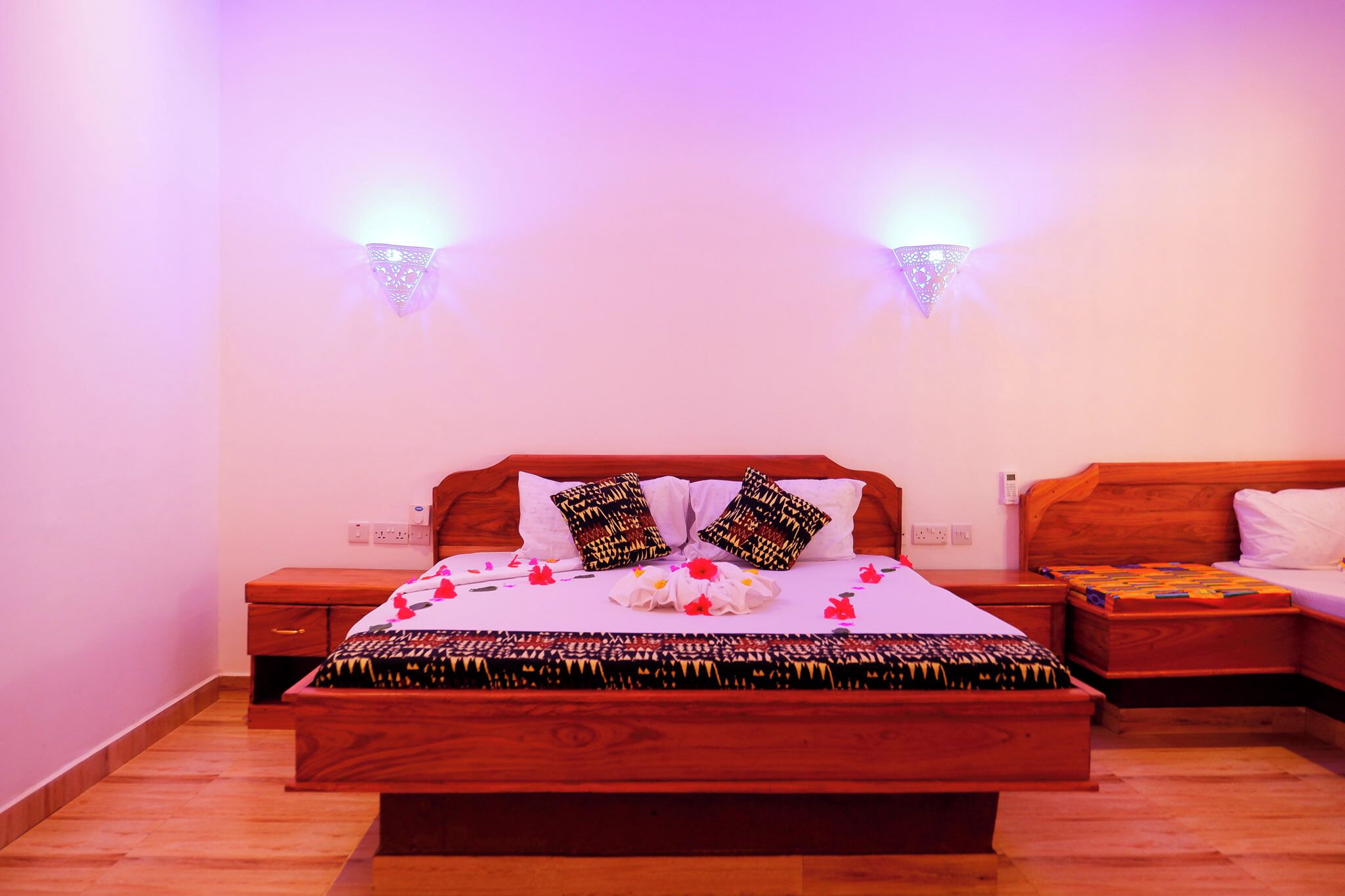 Una cama bien hecha con almohadones estampados, una mesita de noche y un buró.